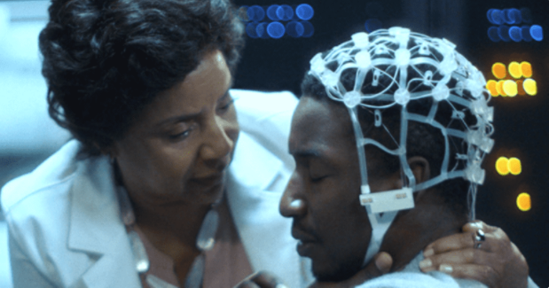 Mamoudou Athie as photographer Nolan Wright, with a white scientific device on his head. Neuropsychiatrist Dr. Lillian Brooks (Phylicia Rashad) is by his side reassuring him.