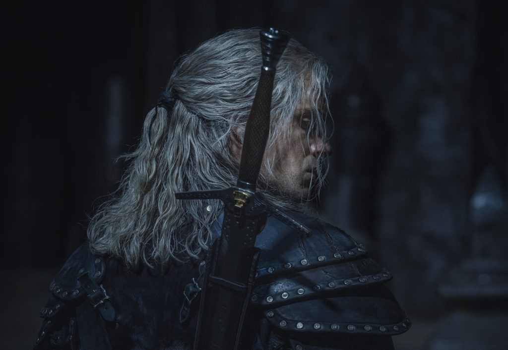 Henry Cavill in a new black suit of armour with a sword on his back, as Geralt of Riveria from The Witcher